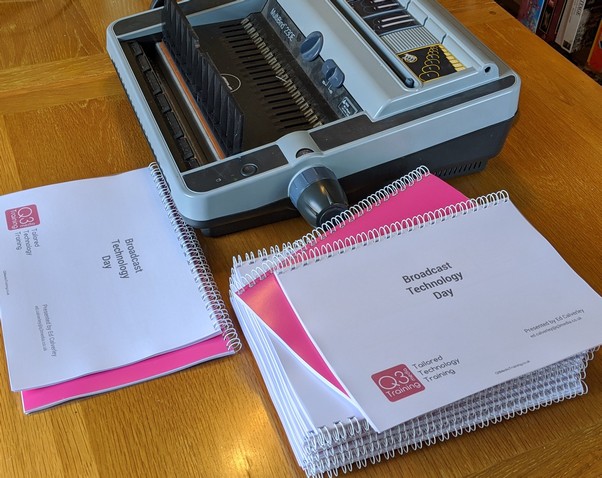 Binding Machine A slack of slide books in ladscape orientation sat on a table in front of a binding machine