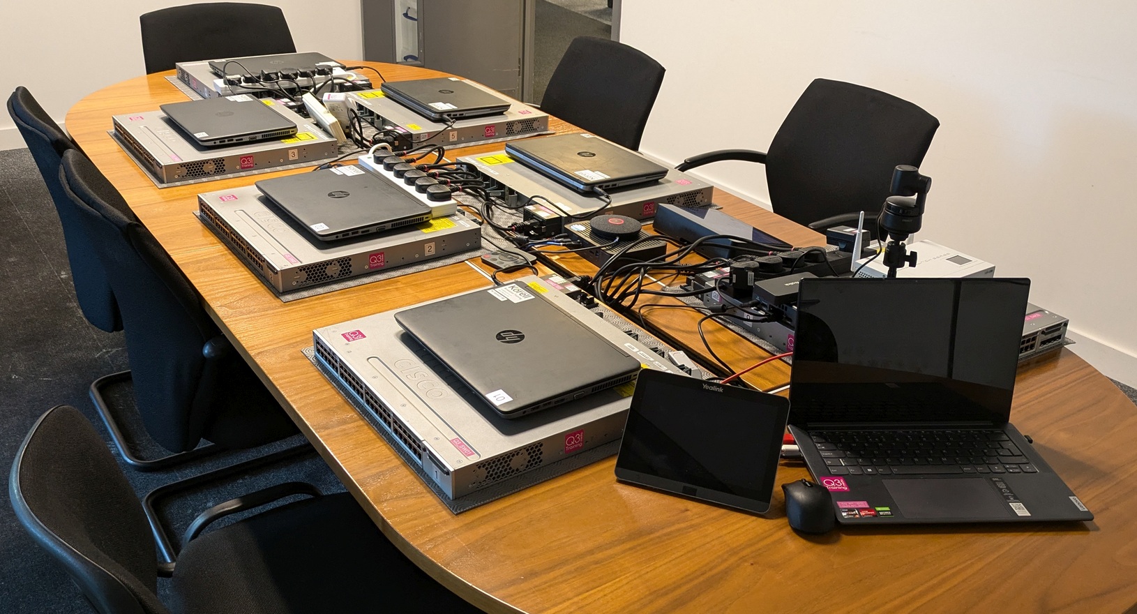 Pracktical - Practical Networking Tidy A meeting room table (no people) covered with network switches, each switch has a laptop on top of it.