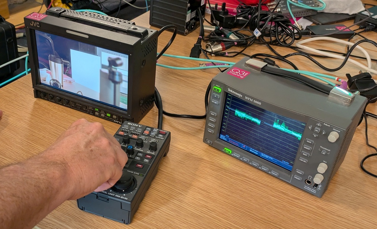 Practical - Broadcast Camera Alignment 2 Tek waveform monitor and portable JVC monitor showing video from camera as someone's hand can be seen adjusting exposure on a remote control panel