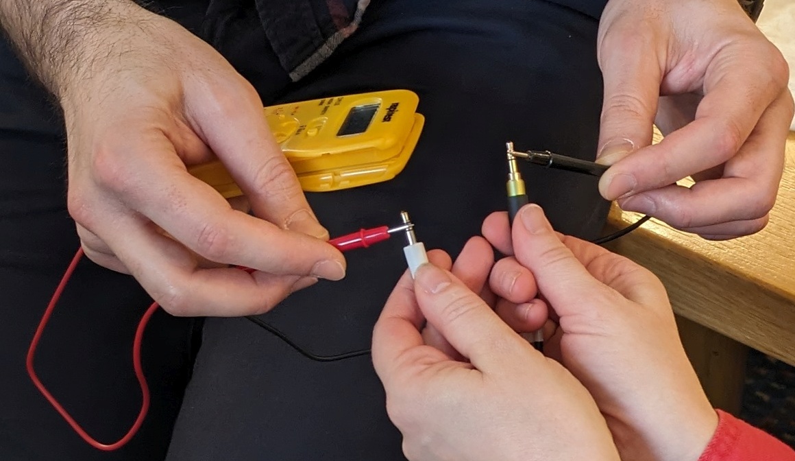 Practical Kit - Audio Wiring Check with Multimeter Closeup of 2 peoples hands performing a continutiy test on a faulty 3.5mm audio cable